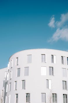 A curved apartment building with a minimalist design against a blue sky.