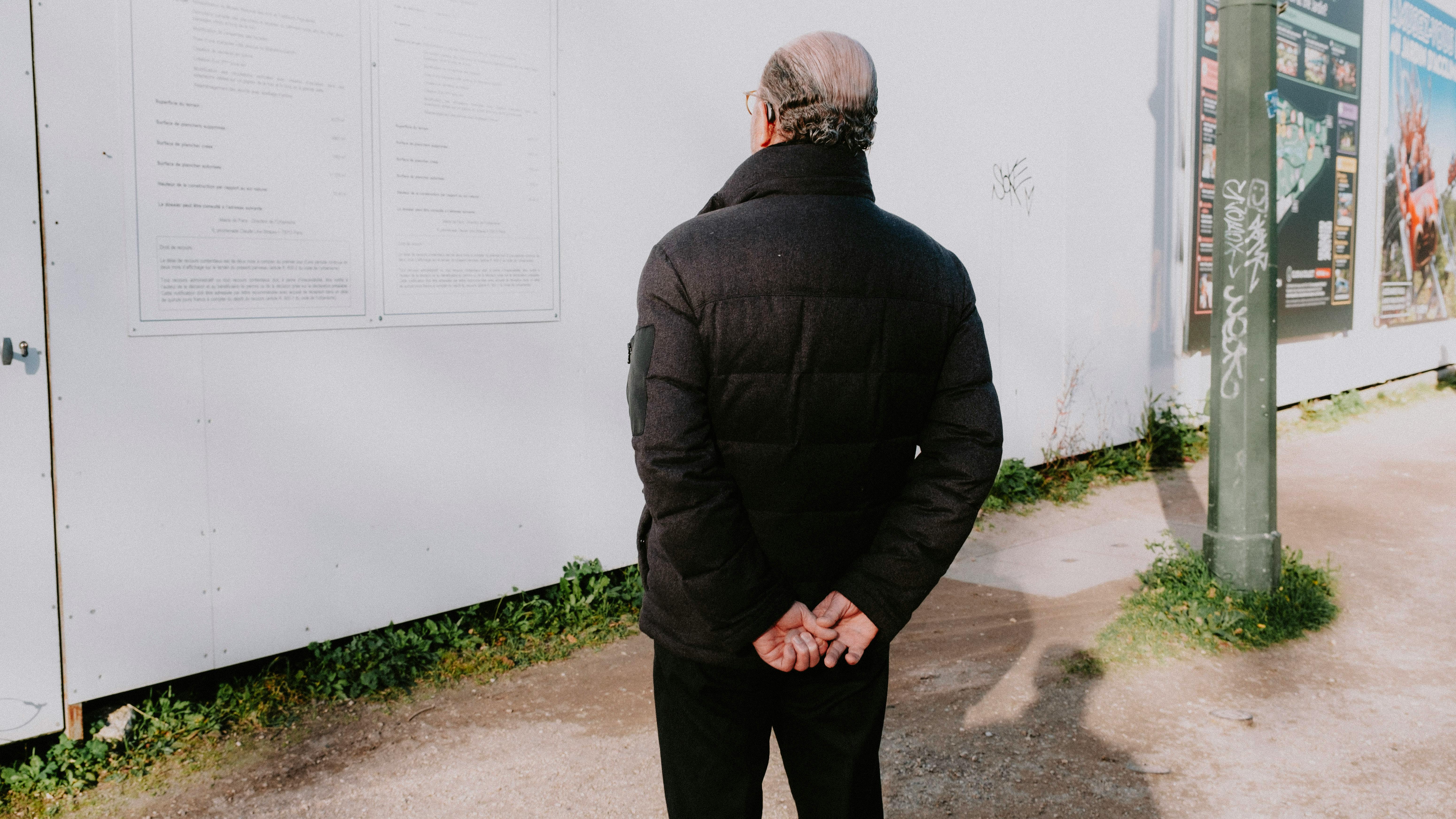 Senior man in winter jacket standing outdoors, viewing wall posters.