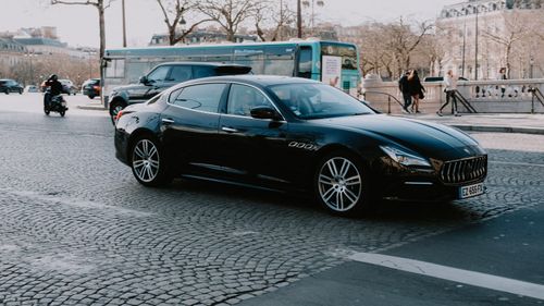 Free Sleek black car driving on a European city street in daylight, capturing elegance and urban life. Stock Photo