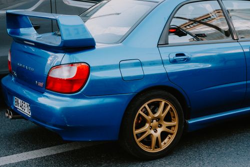 Free Close-up of a blue sports sedan with a prominent spoiler and golden wheels. Stock Photo