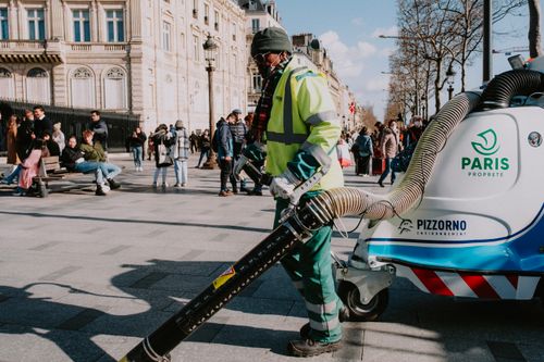Free Paris street cleaner operating equipment, showcasing urban cleanliness amidst city life. Stock Photo