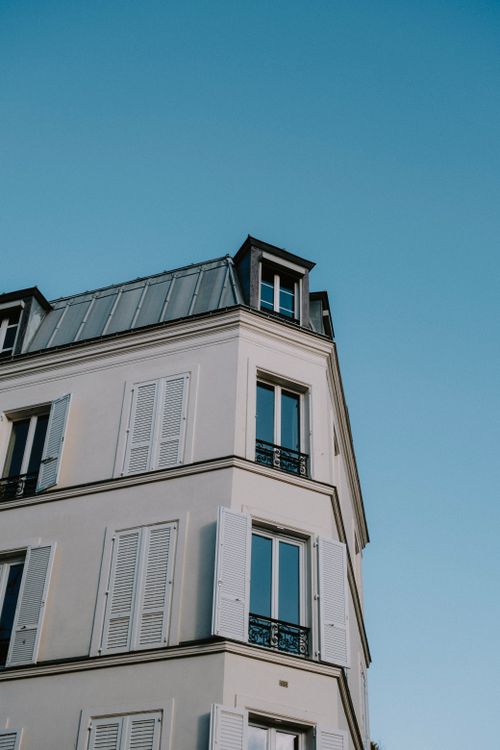 Free Low angle view of a classic French building with open windows and clear blue sky backdrop. Stock Photo