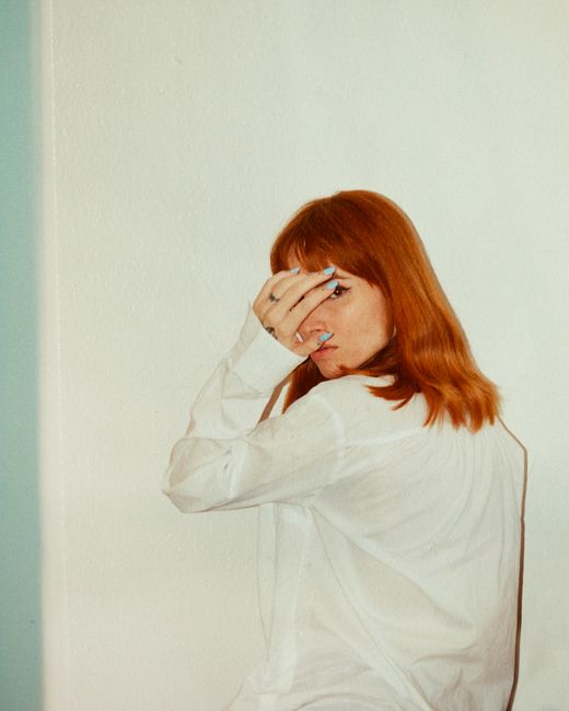 Fashion portrait of a woman half-covering her face with her hand, wearing a white shirt.