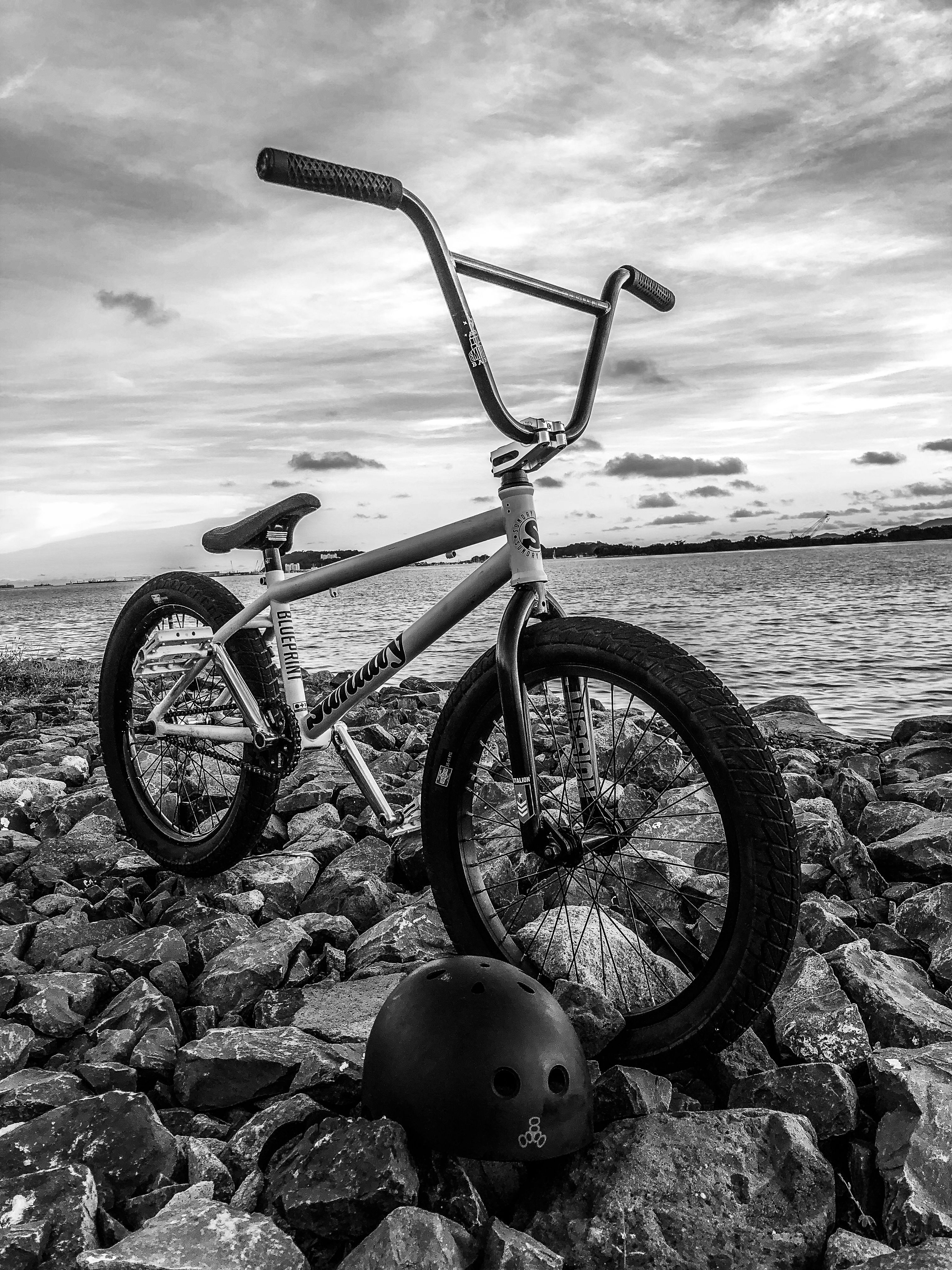 BMX bike parked on rocky shore with helmet, under cloudy sky at a lake.