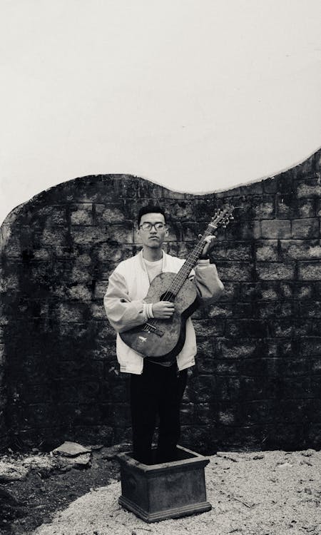 Grayscale  Photo of a Man Standing in a Box Holding Guitar