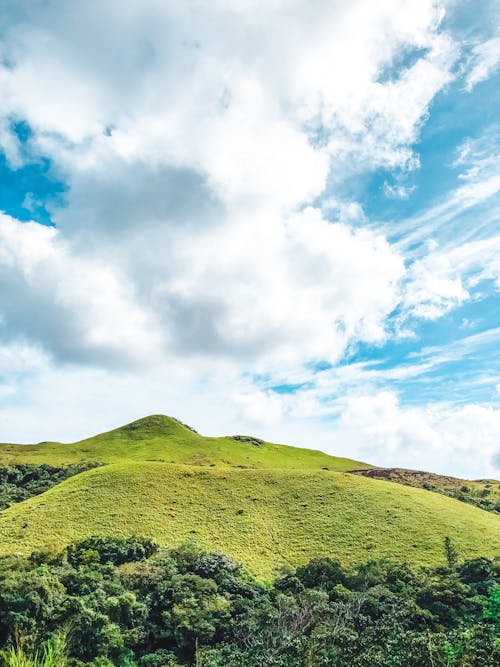 A Green Hill Under a Cloudy Blue Sky