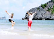 两个人在热带海滩愉快地度过了一天，那里有清澈的蓝色海水和岩石悬崖