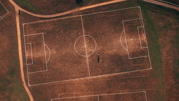 Aerial view of an empty rustic soccer field with a solitary person, showcasing detailed grass lines.