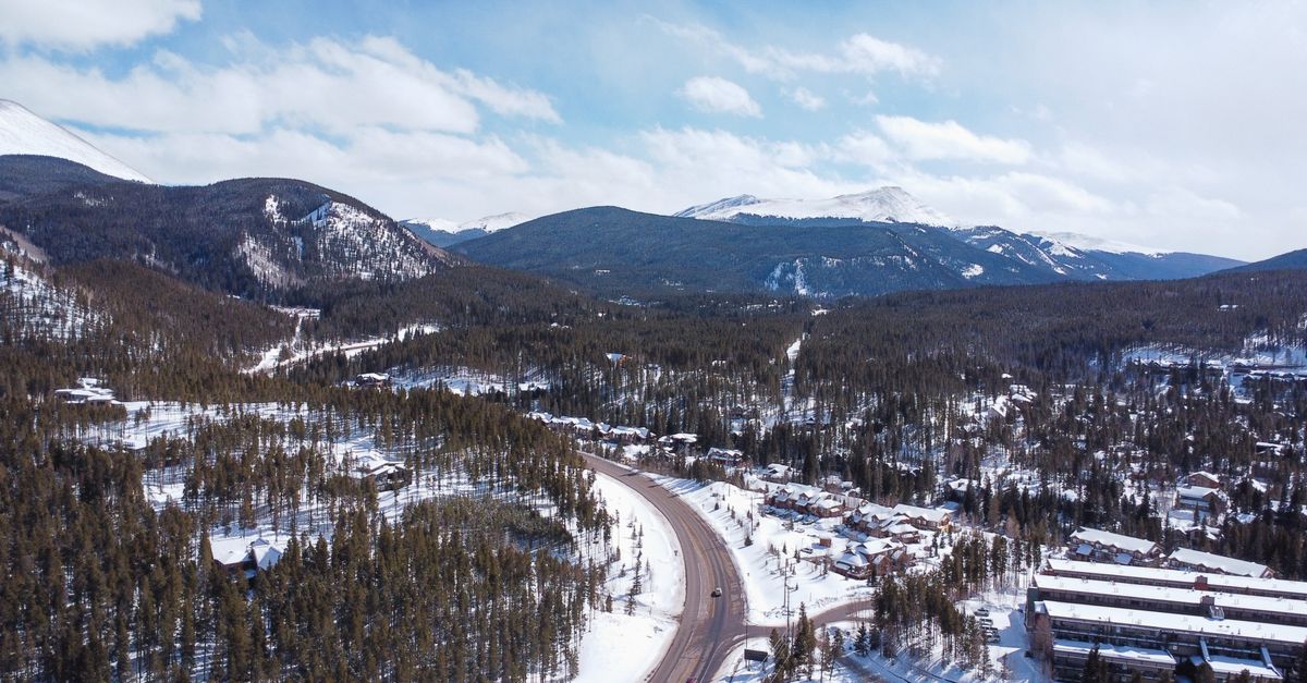 A breathtaking aerial view of a snow-covered mountain road winding through evergreen forests in winter.