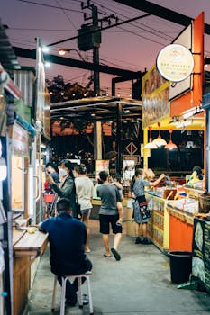 Explore the vibrant atmosphere of a Bangkok night market with people, food stalls, and colorful lights.