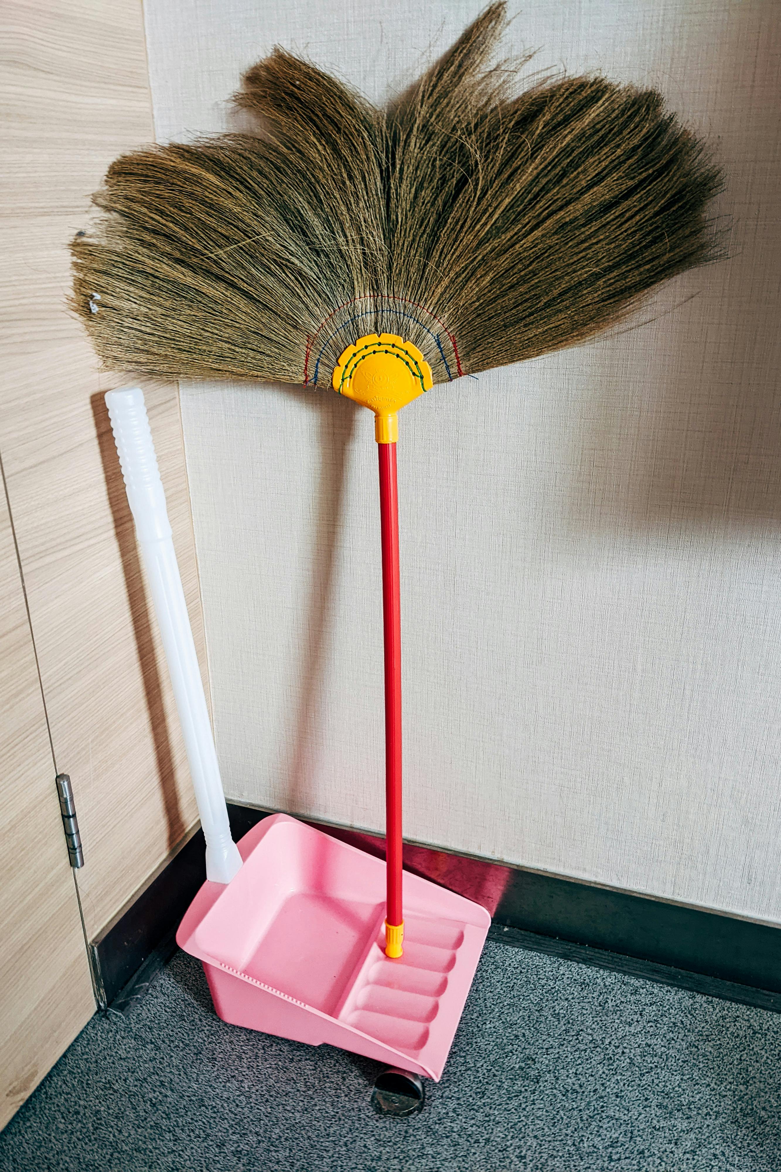 Free A vibrant yellow broom and pink dustpan set against a light wall in Bangkok, Thailand. Stock Photo