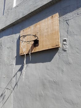 Weathered basketball hoop on a rough wall under bright sunlight.