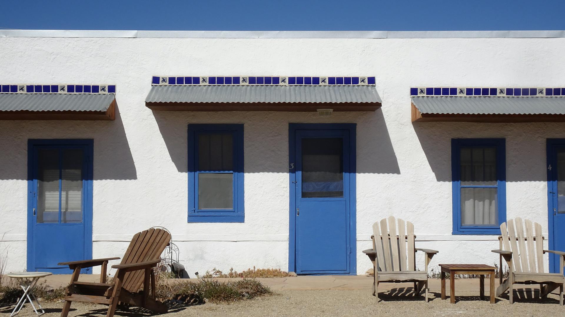 Blue doors and wooden chairs under bright sunlight at a New Mexico motel.