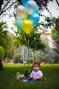 可爱的宝宝坐在风景秀丽的公园草地上，身边有五颜六色的气球