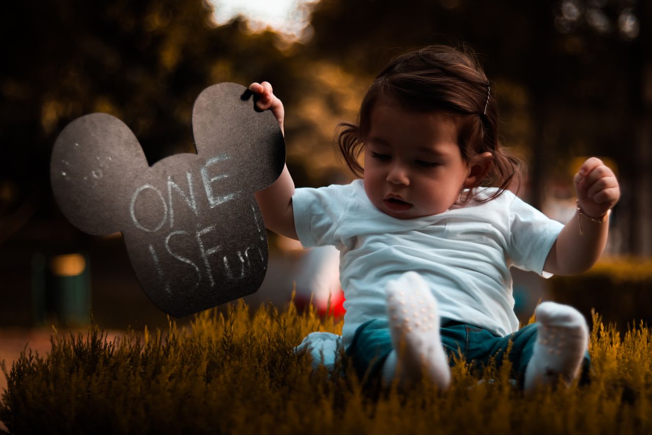 cute baby playing outdoors holding a mickey mouse shaped sign at sunse