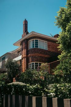 A picturesque brick house surrounded by lush greenery under a bright blue sky, capturing serene residential architecture.