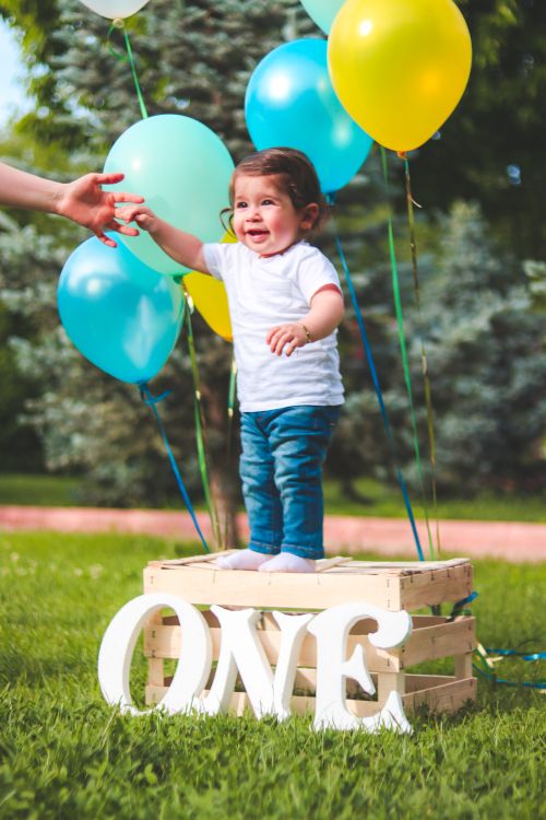 Free Smiling toddler celebrating first birthday outdoors with colorful balloons. Stock Photo