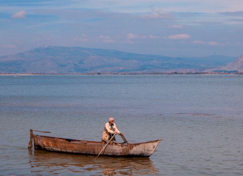 A lone boatman paddles an old wooden boat on a serene lake in Denizli, Türkiye, under a clear sky.