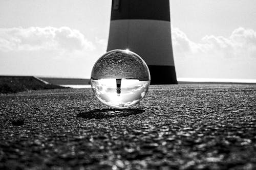 A Grayscale of a Crystal Ball on the Ground with a Reflection of a Lighthouse