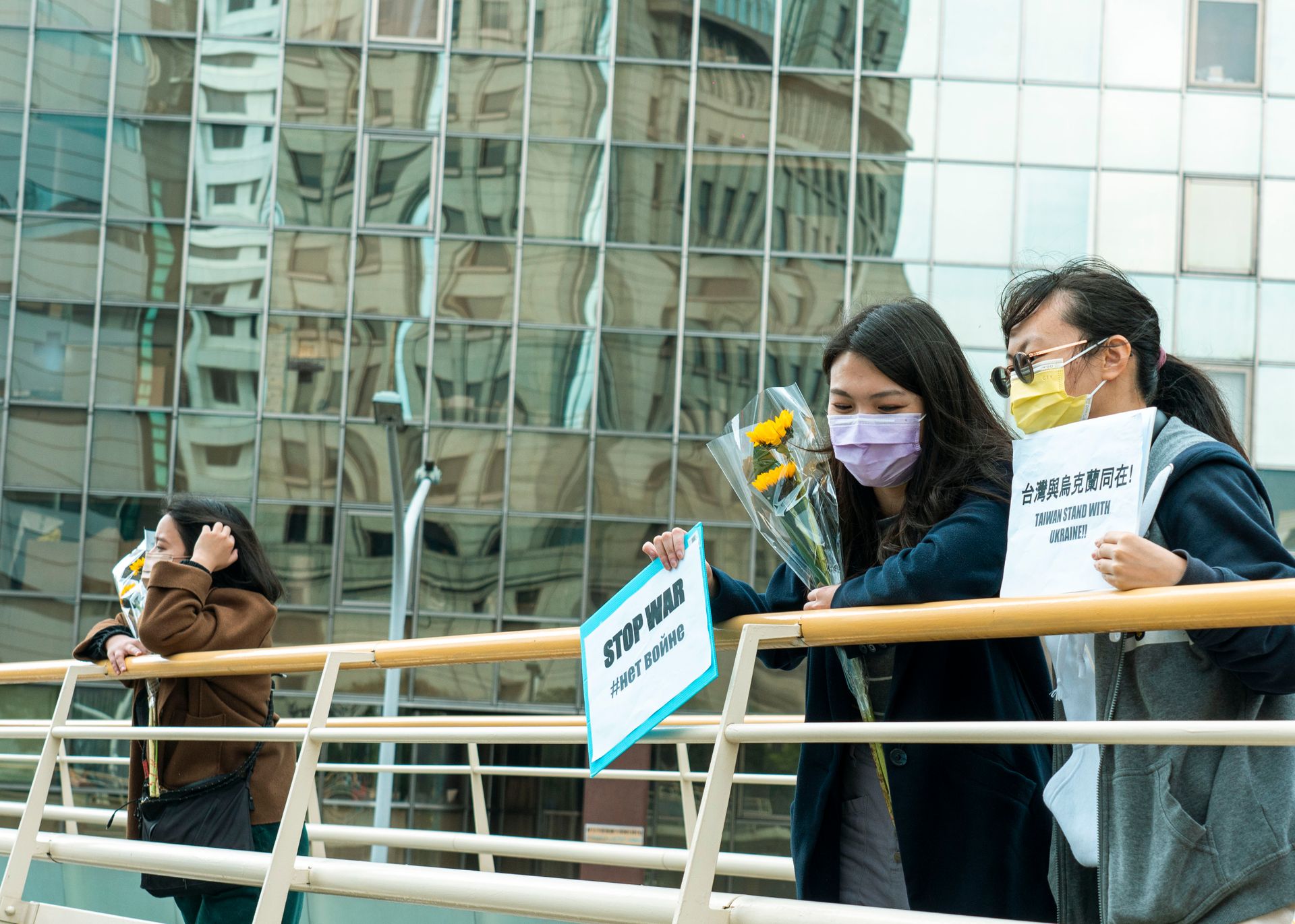 Two women peacefully protesting with signs and flowers on a bridge.