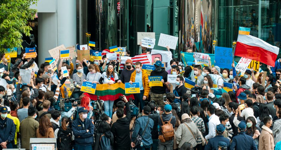 A large protest with diverse participants holding flags and signs advocating for peace and unity.