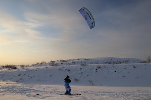 Person snowkiting on a snowy landscape in Kirovsk, Russia during winter sunset.
