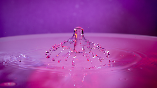 Free Close-up of a mesmerizing water drop splash with vibrant, purple background. Stock Photo