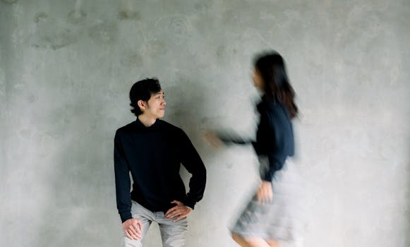 Artistic photo capturing blurred motion of a woman walking past a seated man indoors.