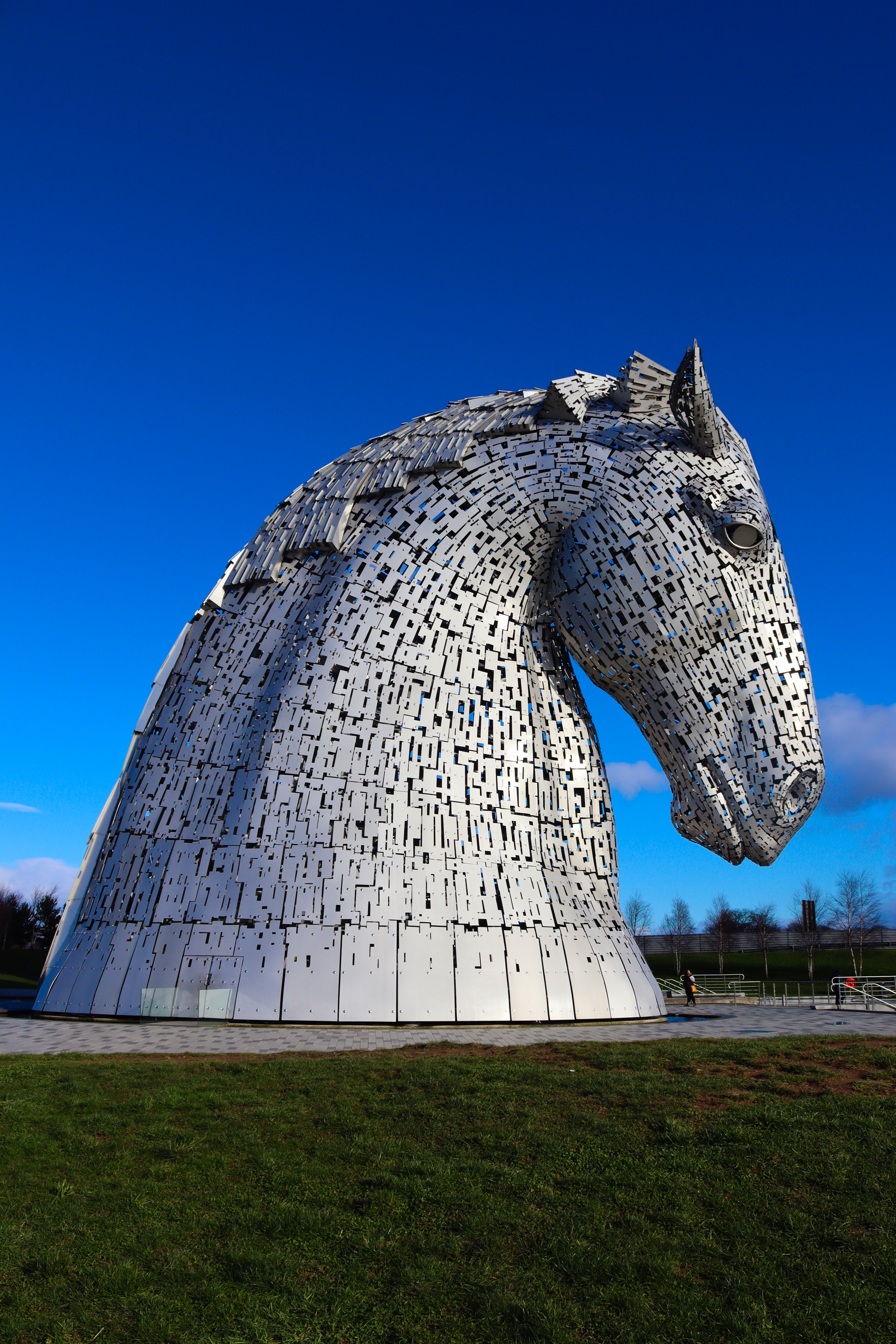 Majestic horse head sculpture 'The Kelpies' in Falkirk, Scotland, under a clear blue sky.