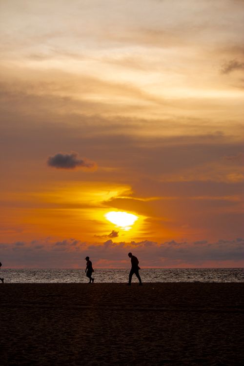 Free Peaceful beach scene in Angola with silhouettes of people and a stunning sunset reflecting over the ocean. Stock Photo