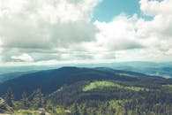 一座惊人的山脉与茂密的森林上空，戏剧性的多云天空笼罩着