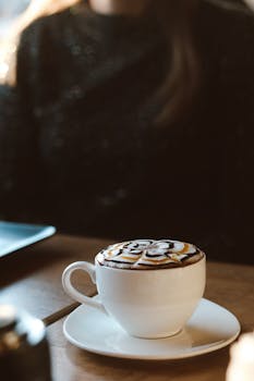 Close-up of a decorated coffee cup on a wooden table with a blurred background indoors.