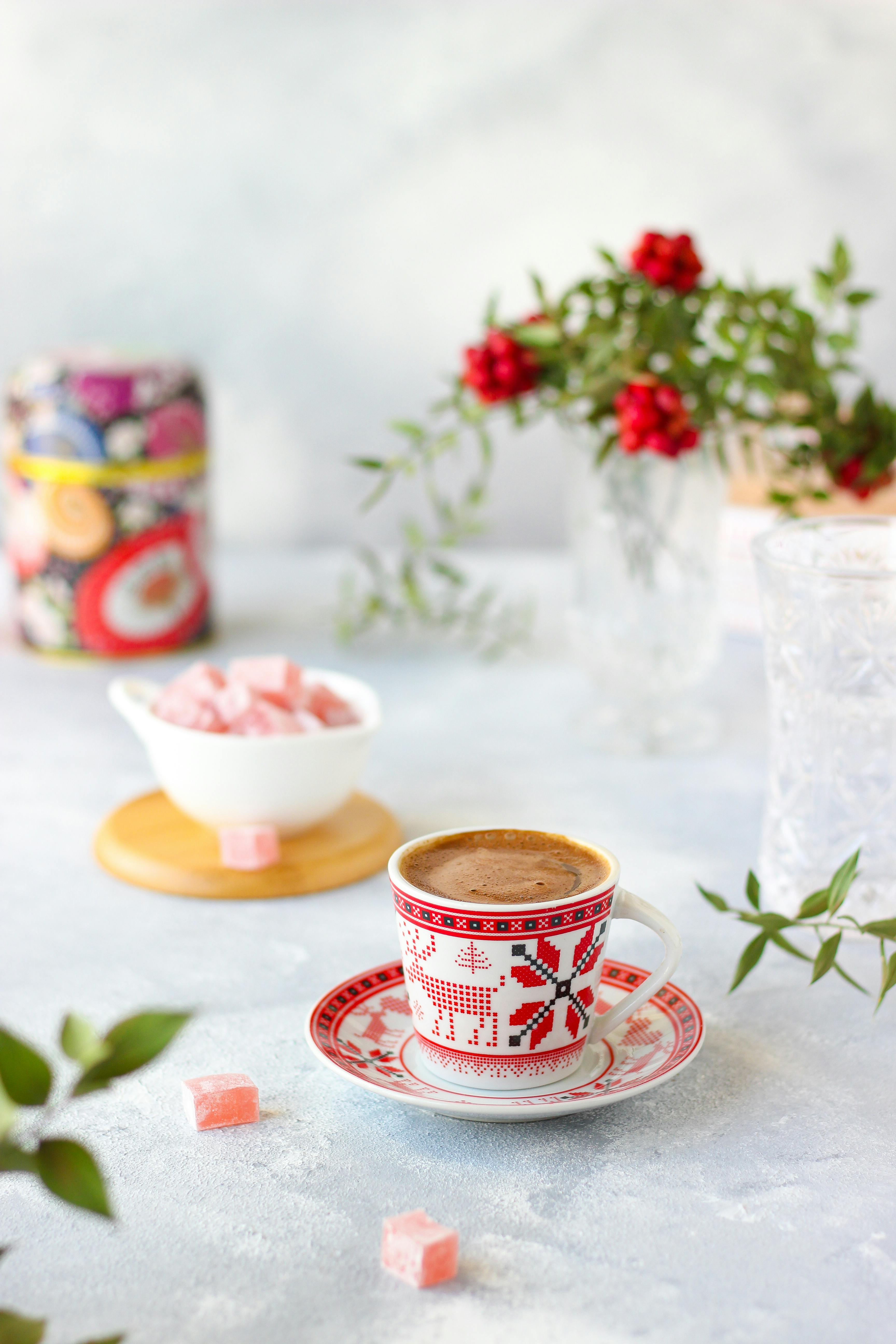 Bright coffee cup with festive patterns, surrounded by flowers and cubes on a light table.