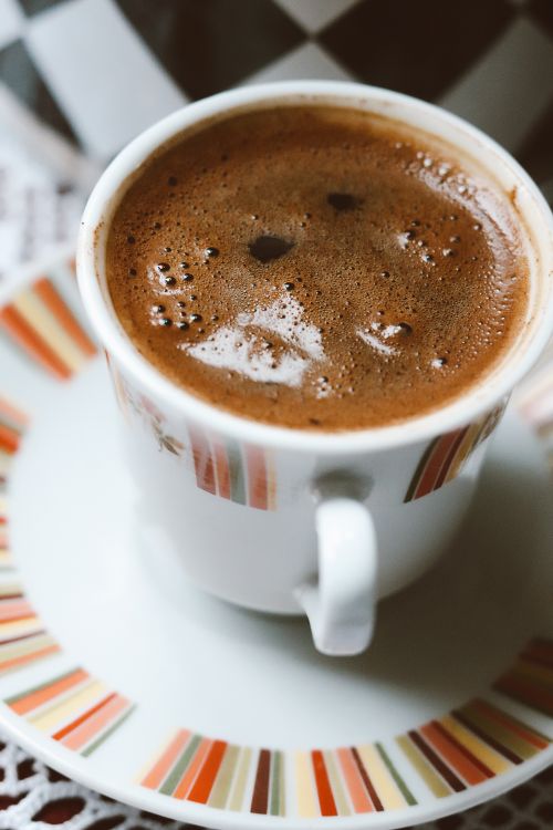 Free A close-up shot of a steaming cup of coffee with bubbles in a decorative cup and saucer. Stock Photo