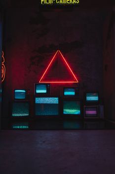 Retro televisions under neon lights in a dark room, creating a vintage ambiance.