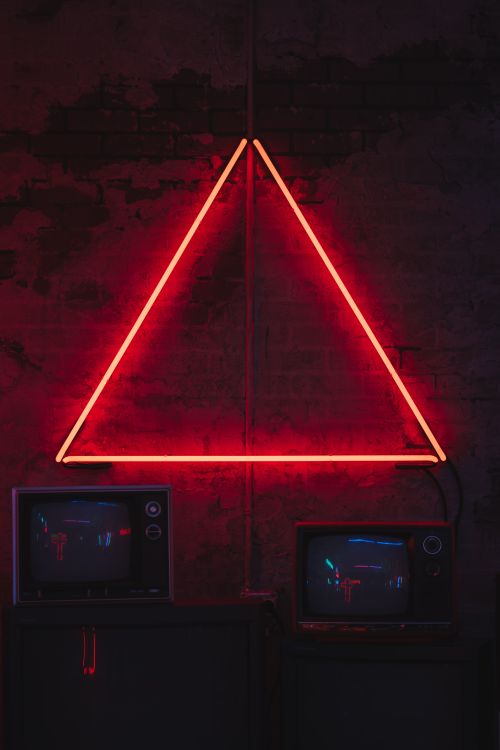 Free A vibrant neon triangle glows over vintage TVs set against a rustic brick wall. Stock Photo