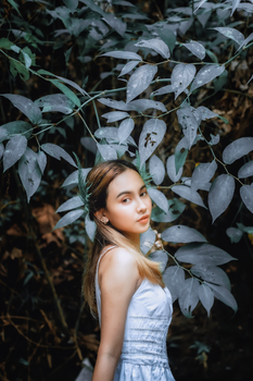 Portrait of a young woman in a serene natural setting, surrounded by lush green leaves.