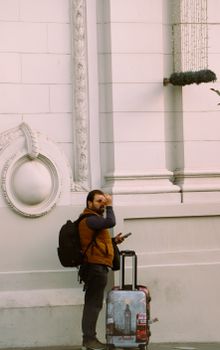 Man standing outdoors with backpack and luggage, looking at smartphone outside a building in Istanbul.