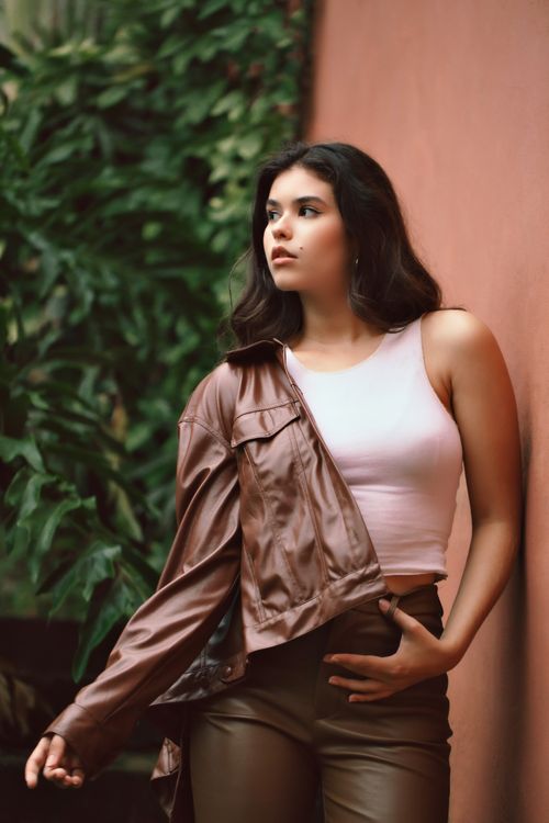 Free Fashionable woman in tank top and brown leather jacket posing against a textured wall. Stock Photo