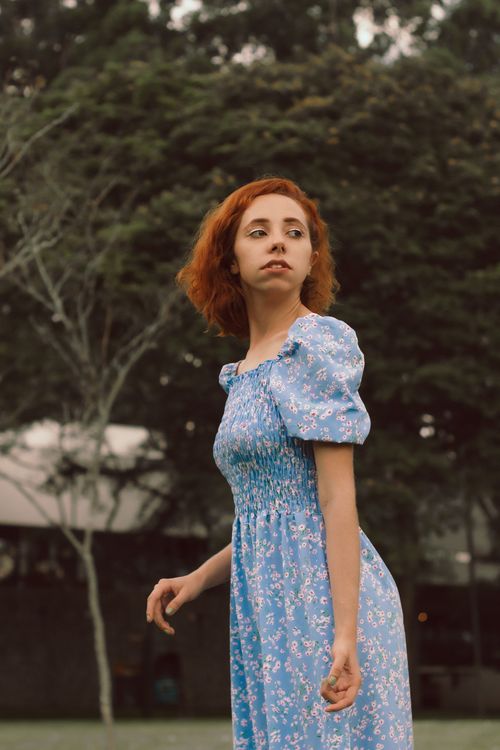 Free Portrait of a young woman with auburn hair in a blue floral dress outdoors. Stock Photo