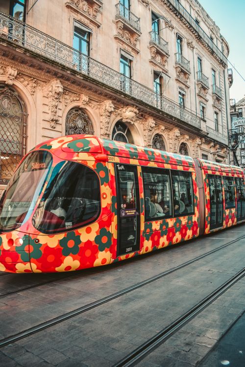 Free A vibrant flower-patterned tram travels on a city street in Montpellier, France. Stock Photo