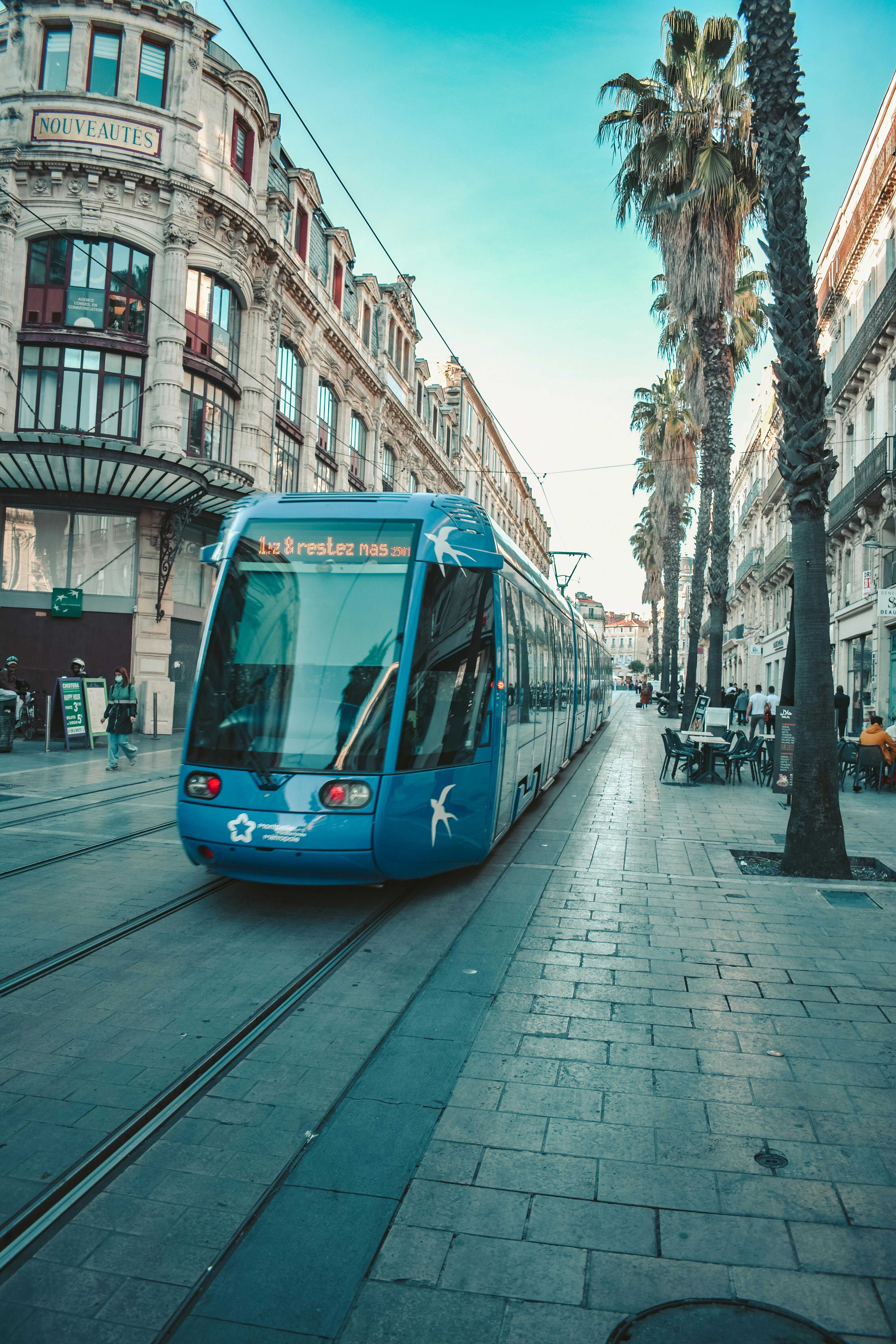 Free Blue tram on sunlit street in Montpellier, showcasing the city's charming urban landscape. Stock Photo