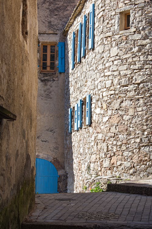View of a Narrow Alley between Buildings with Stone Walls and Blue Window Shutters