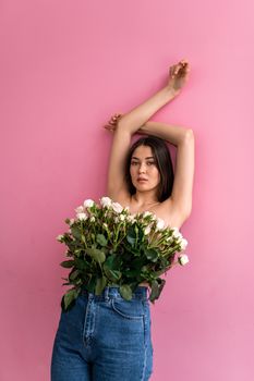 Artsy portrait of a woman embracing nature with roses in her jeans against a pink backdrop.