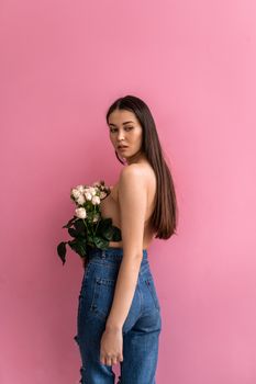 Portrait of a stylish woman in jeans holding roses against a pink background, exuding elegance and femininity.