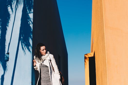 一位穿着时尚服装的女子，在明亮的阳光下，对着五颜六色的现代建筑摆着姿势