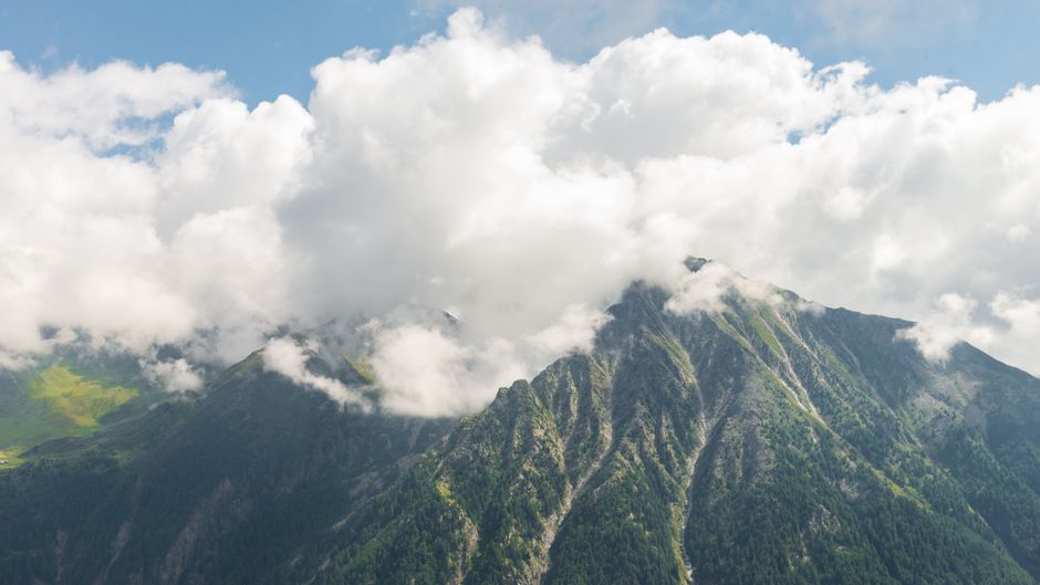 Fotomural Vista escénica de picos montañosos cubiertos de nubes bajo un cielo brillante.