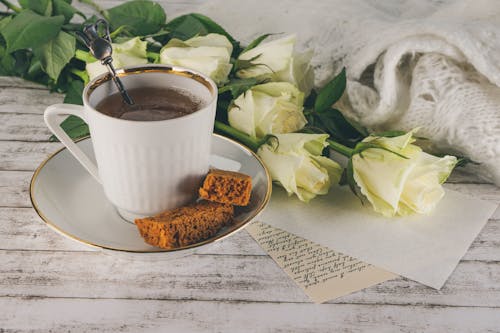 A Cup of Coffee with a Sweet Snack and Roses on a Table