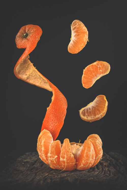 Free Creative image of tangerine segments and peel suspended against a dark background, highlighting freshness. Stock Photo