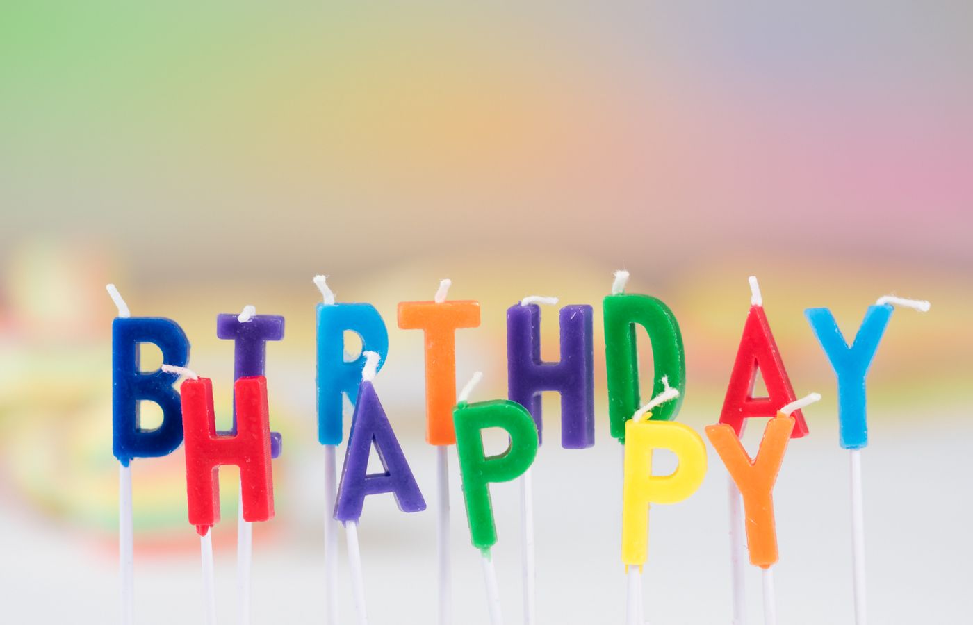 Vibrant birthday candle letters spelling 'Happy Birthday' with a colorful blurred background. Perfect for celebration visuals.